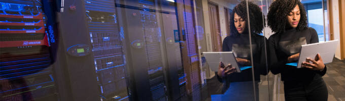 Woman leaning up against glass with computer equipment behind it