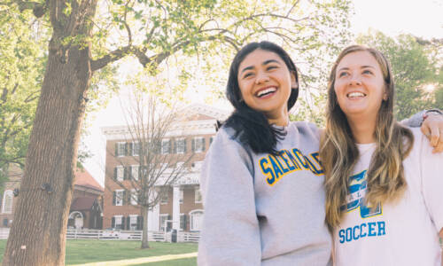 Two Salem College students smiling in front of Main hall on campus
