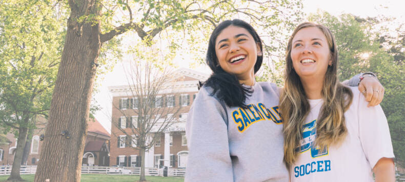 Two Salem College students smiling in front of Main hall on campus