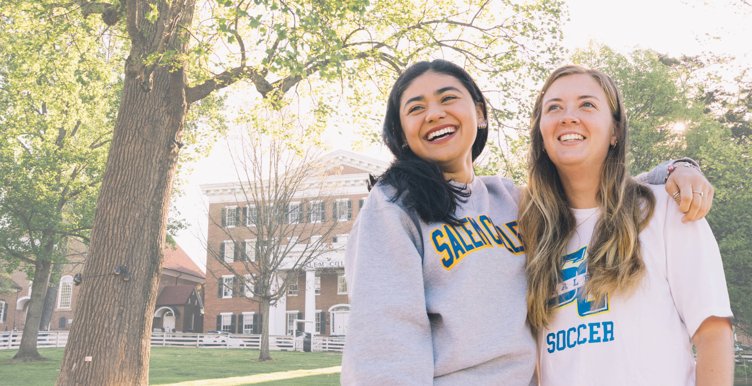 Two Salem College students smiling in front of Main hall on campus